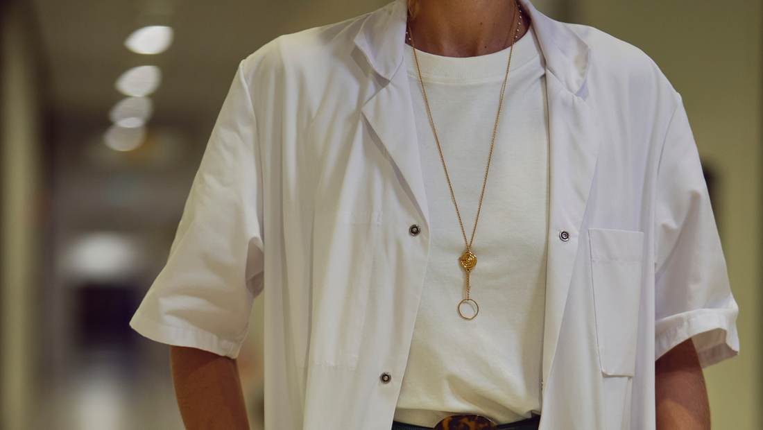 Collier porte-bague Aphrodite porté sur une blouse blanche dans un couloir d'hôpital